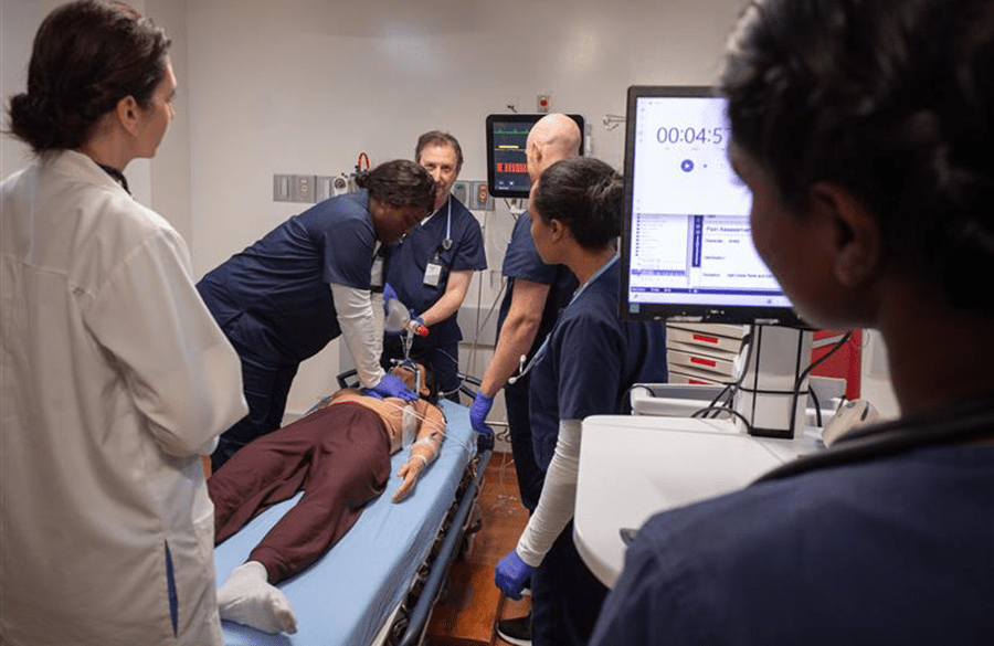Healthcare professionals perform CPR on a simulation mannequin in a training room, focusing on teamwork and emergency response skills.
